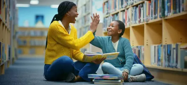 Library, girl and teacher high five for education goal, learning and celebration for storytelling. Educator, black woman and kid on floor for fun, fantasy stories and language development or relaxing